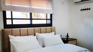 Un dormitorio con cama, mesita de noche, ventana con persianas y un equipo de aire acondicionado.