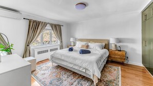 Una camera da letto con un letto, comodini, un tavolo da notte, un termosifone, una finestra con tende e un'armadio verde.