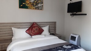 En snyggt bäddad säng med vita och mönstrade sängkläder, en röd prydnadskudde och en väggmonterad TV.