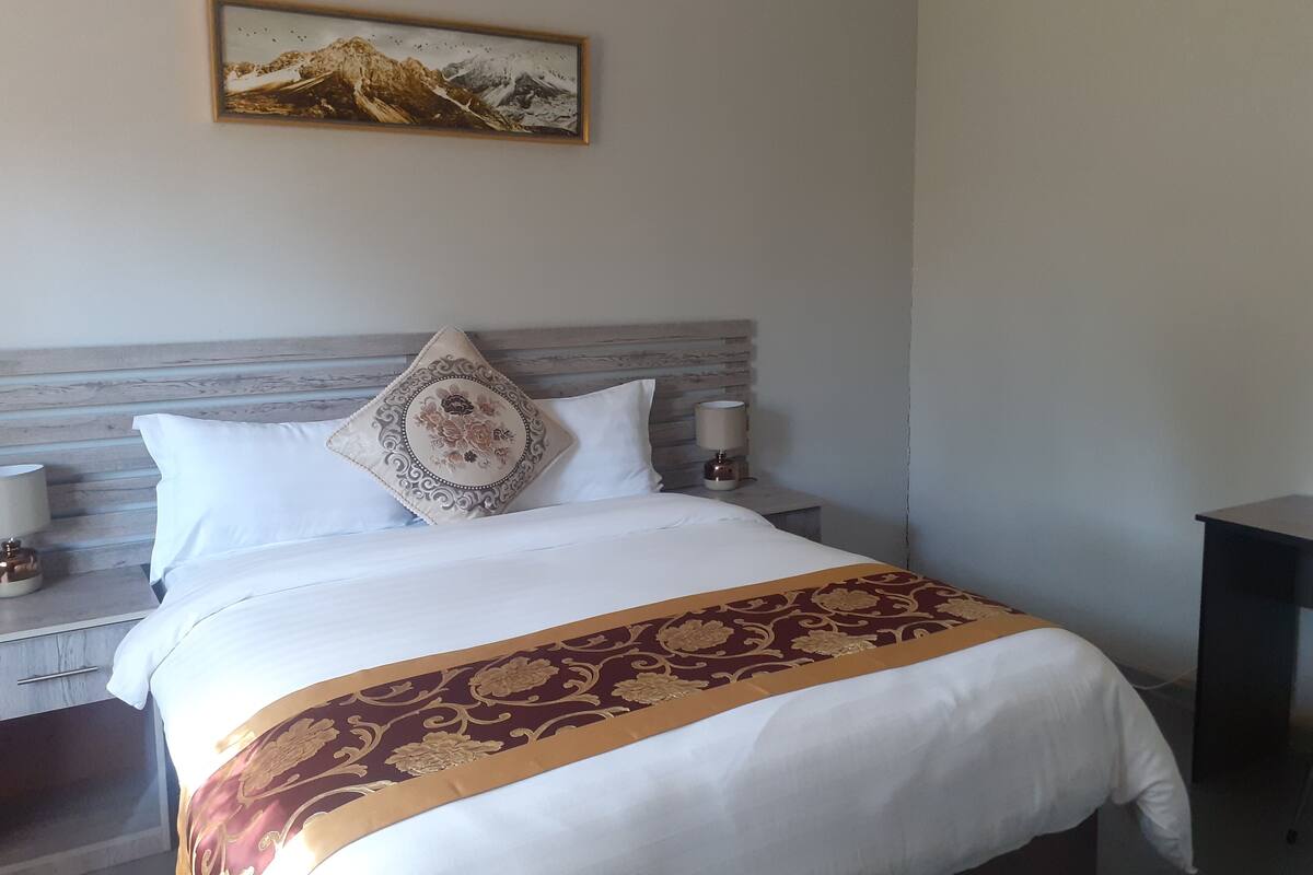 Una cama bien tendida con una colcha estampada, un cojín decorativo y un cuadro colgado en la pared.