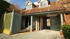 Une maison à deux étages, avec un toit en tuiles, une véranda et une cour clôturée.