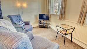 Un salon avec un canapé, un fauteuil et une petite table en verre sur laquelle repose un livre.