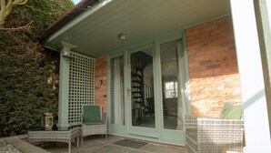 Une terrasse couverte, dotée de meubles en osier, d’un mur en briques et d’une porte vitrée donnant sur un espace intérieur.