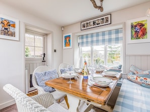 Comedor con una mesa de madera dispuesta para cuatro personas, rodeado de sillas de mimbre.