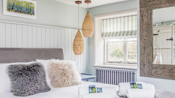 A bedroom with a bed, two hanging wicker lamps, a radiator, and a window with a striped curtain.