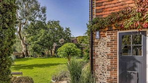 A house with a stone facade, a dark door, and a well-maintained garden with a lawn, a stone pathway, and various plants.