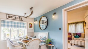 A dining area with a checkered window blind, a 'WELCOME' sign, a round mirror, and a dining table with chairs.