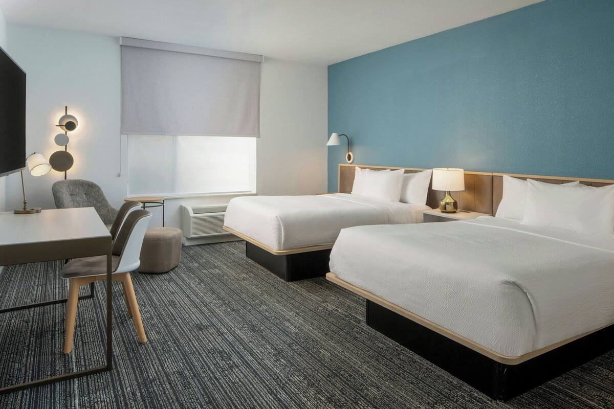 Een hotelkamer met twee bedden, een bureau, een stoel, een televisie en een lamp.