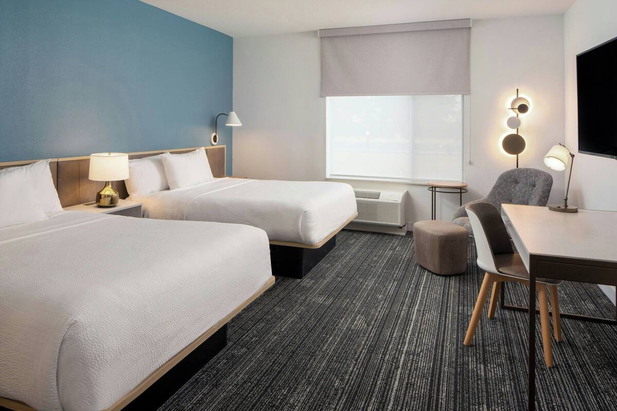 Een hotelkamer met twee bedden, een bureau, een stoel, een lamp, een televisie en een raam met uitzicht.