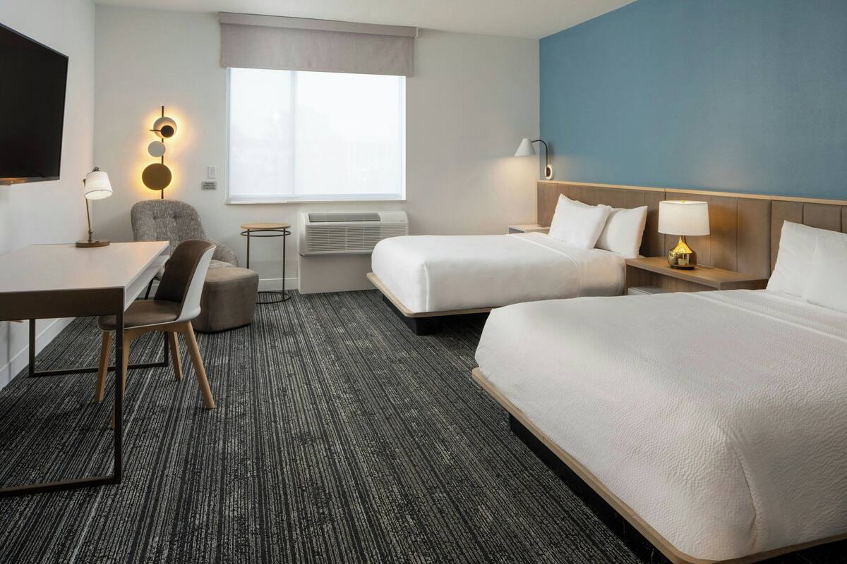 Een hotelkamer met twee bedden, een bureau, een stoel, een televisie en een raam met gordijnen.