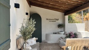 A cozy entrance with a green door, a sign reading "Maison Gigi BED & BREAKFAST", a potted plant, and a wooden bench. - B&B Maison Gigi (La Garde-Freinet)