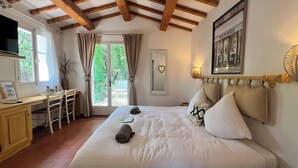 A hotel room with a bed, a desk, and a chair. There is a window with curtains, a mirror, and a framed picture on the wall. - B&B Maison Gigi (La Garde-Freinet)