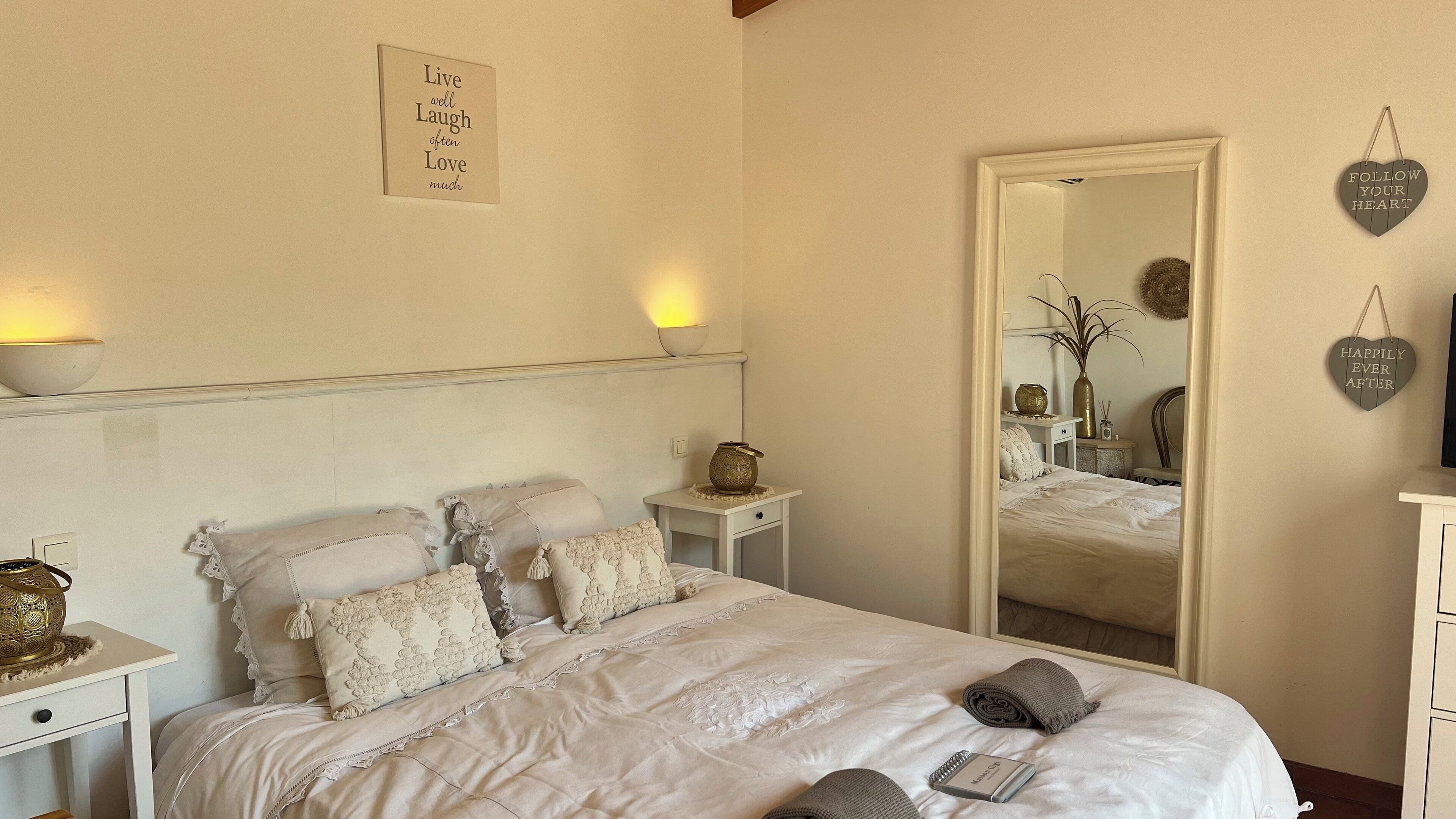 A neatly arranged bedroom with a large mirror, a bedside table with a lamp, and decorative pillows.