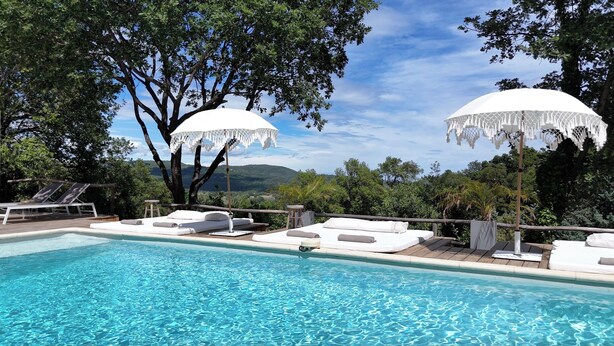 A pool area with lounge chairs and umbrellas, surrounded by trees and a view of the landscape. - B&B Maison Gigi (La Garde-Freinet)
