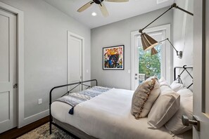 A bedroom with a bed, a ceiling fan, a window with a view, and a painting on the wall. - South Lamar Wellness Haven / Sauna / Hot Tub / BBQ (Austin)