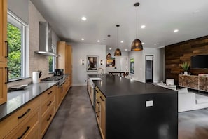 A modern kitchen with a central island, wooden cabinets, and pendant lighting. - South Lamar Wellness Haven / Sauna / Hot Tub / BBQ (Austin)
