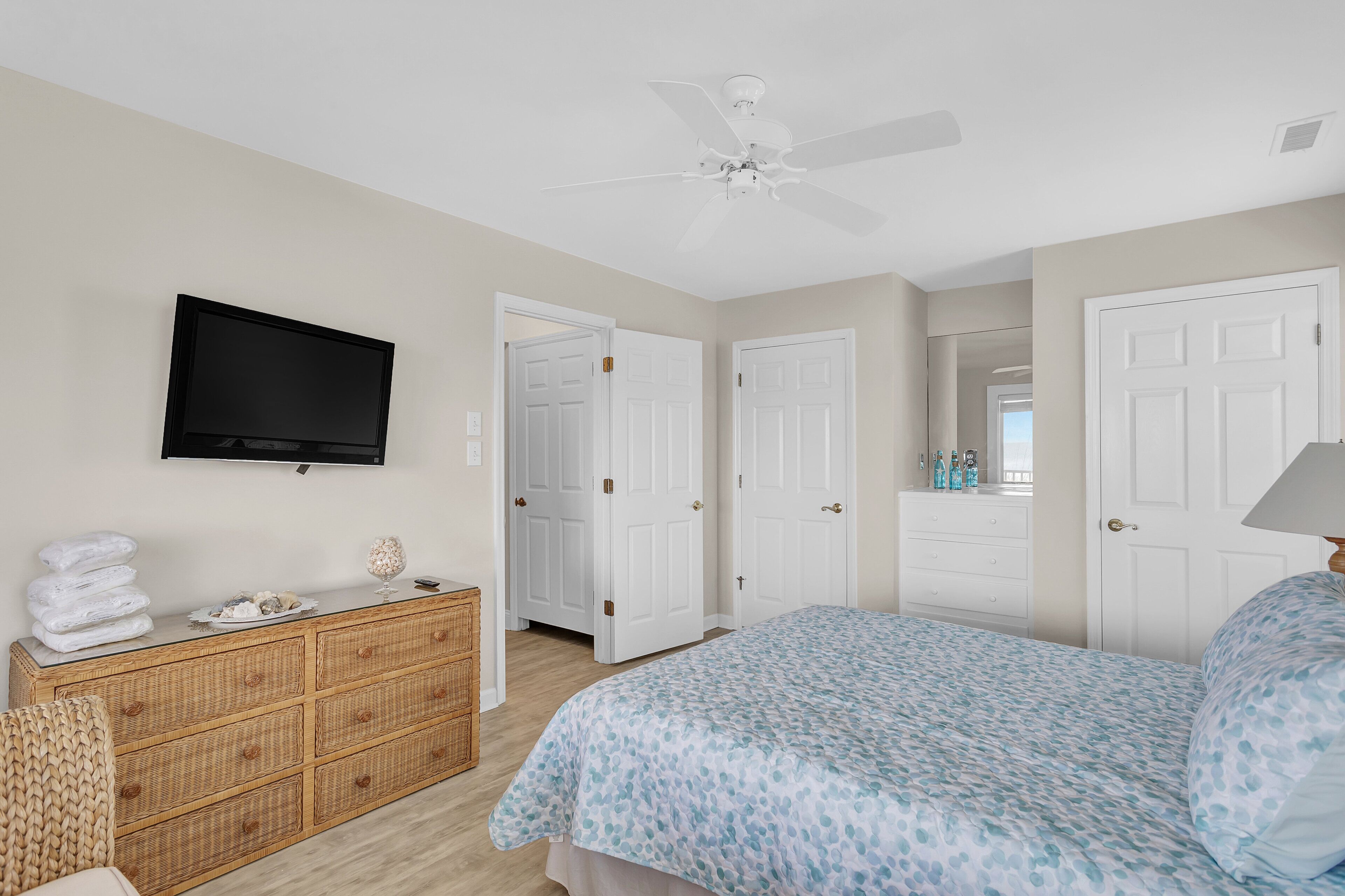 A bedroom with a bed, a television mounted on the wall, a dresser, and a ceiling fan.