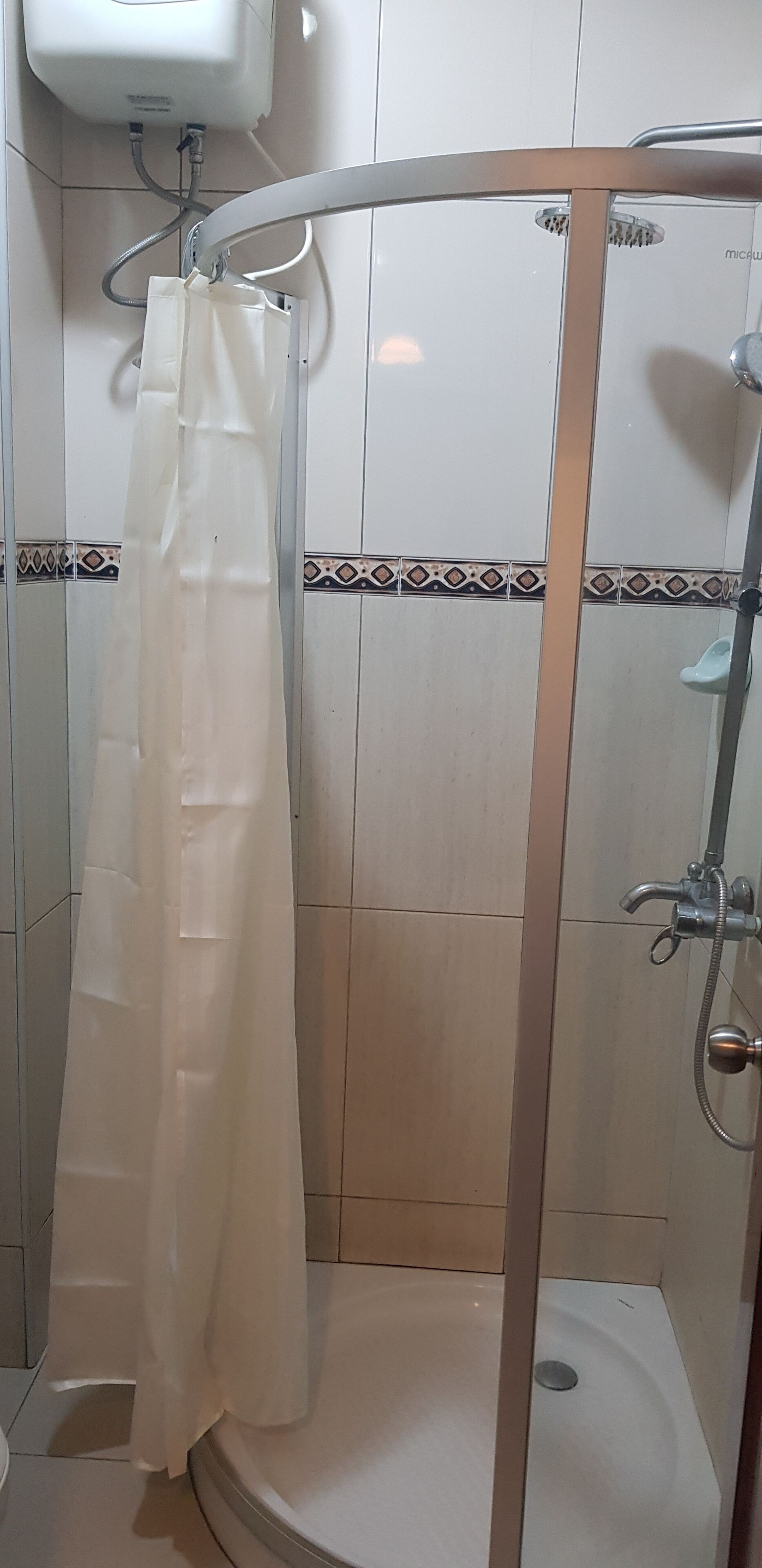 A shower area with a white shower curtain, a handheld showerhead, and a wall-mounted faucet.