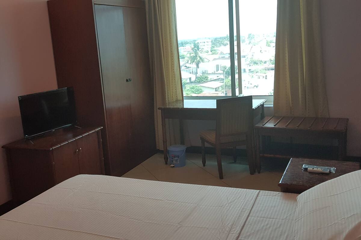Une chambre d’hôtel équipée d’un lit, d’un bureau, d’une chaise, d’une télévision et d’une fenêtre avec des rideaux.