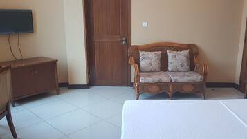 A room with a bed, a wooden cabinet, a wicker sofa, and a television mounted on the wall.