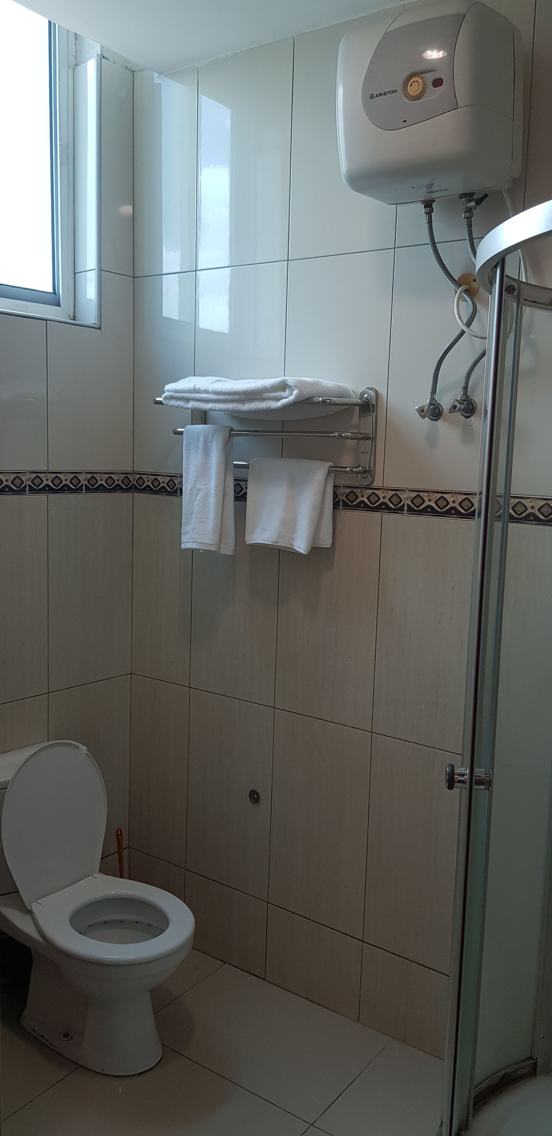 A bathroom with a toilet, a towel rack with towels, a shower, and a water heater.