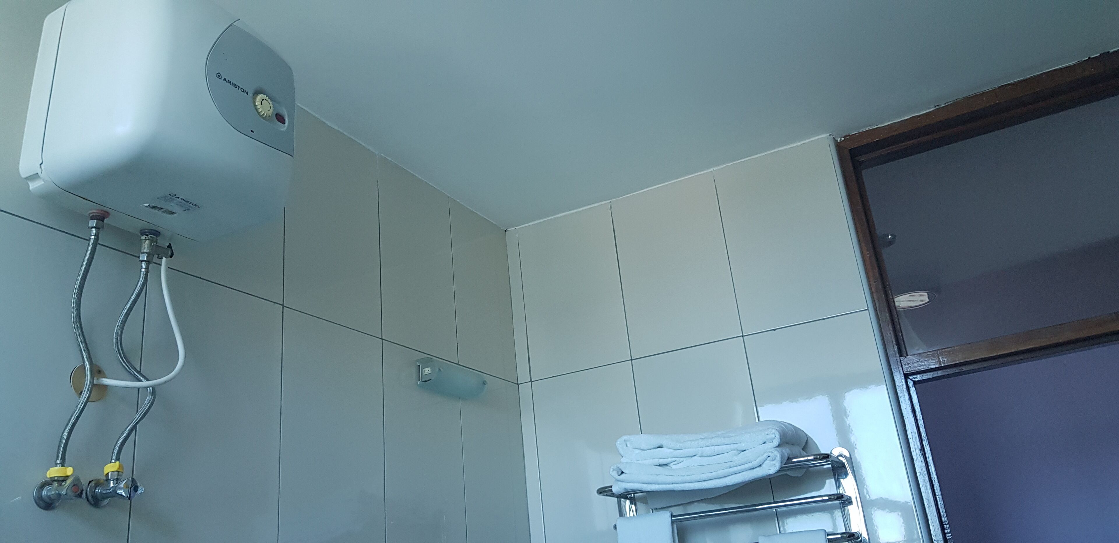 A bathroom with a white shower enclosure, a towel rack with a folded towel, and a visible water heater on the wall.