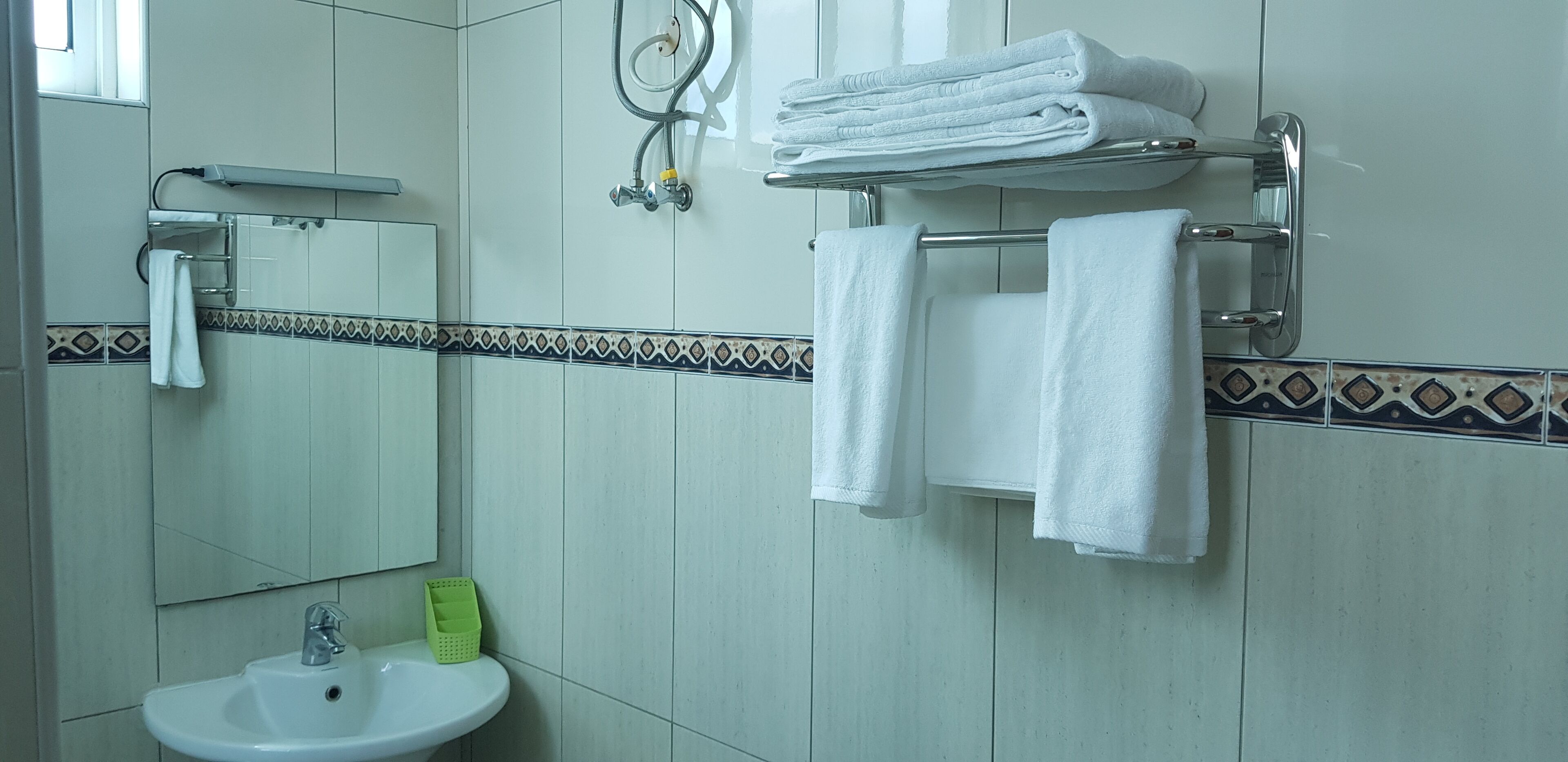 Une salle de bain équipée d’un lavabo, d’un miroir, d’un porte-serviettes avec des serviettes pliées et d’une pomme de douche.