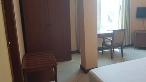 Une chambre d’hôtel comprenant un lit, une chaise en bois, un bureau, une télévision et une armoire.