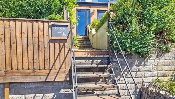 A wooden fence with a sign reading "High Tide" and a set of stone steps leading to a blue door. - 2 bedroom accommodation in Combe Martin (Combe Martin)