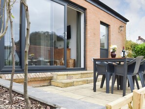 Een terras met een tafel en stoelen, een bakstenen muur en een schuifdeur met glas.