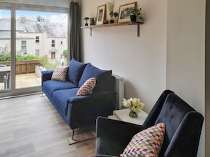 A modern living room with a blue sofa, a smaller armchair, and a white side table with a vase of flowers. - 2 bedroom accommodation in Combe Martin (Combe Martin)