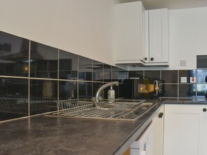 Een moderne keuken met een roestvrijstalen spoelbak, zwart-wit tegels en een magnetron.