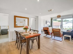 Een eetruimte met een houten tafel voor vier personen, omringd door stoelen, een spiegel en een bloemenvaas.