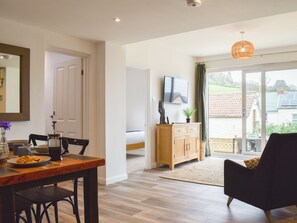 A modern living room with a wooden dining table, a black sofa, and a television on the wall. - 2 bedroom accommodation in Combe Martin (Combe Martin)