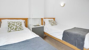 A hotel room with two single beds, a bedside table, a lamp, and a wall-mounted light fixture. - 2 bedroom accommodation in Combe Martin (Combe Martin)