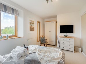 A bedroom with a bed, a dresser, a chair, a television, and a window with a view.