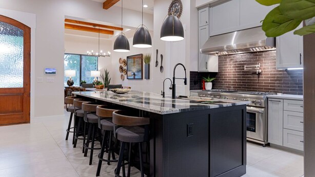 Una cocina moderna con una isla grande, taburetes de bar, iluminación colgante y electrodomésticos de acero inoxidable.