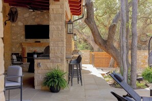 An outdoor patio with stone walls, a flat-screen TV, a grill, and seating areas.