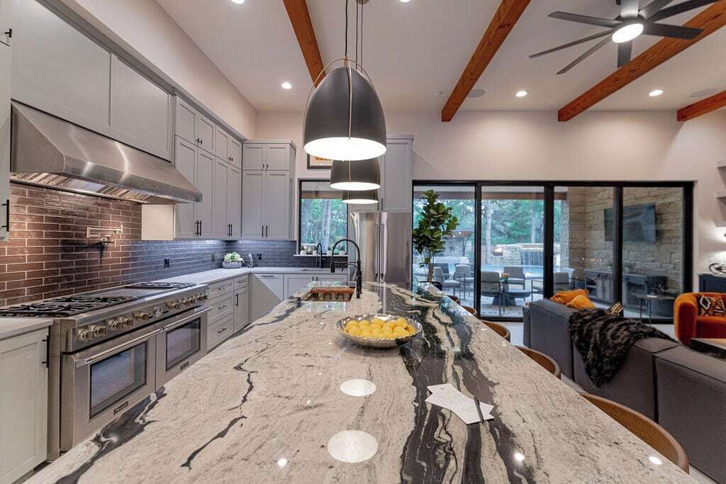 A modern kitchen with a large island, stainless steel appliances, and a dining area with a view.