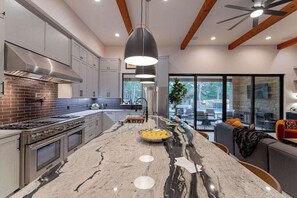 A modern kitchen with a large island, stainless steel appliances, and a dining area with a view. - Luxury Retreat | Near Austin at Always on My Mind (Austin)