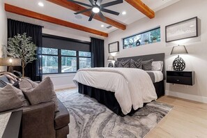 A bedroom with a bed, a nightstand, a lamp, a window with curtains, and a ceiling fan.