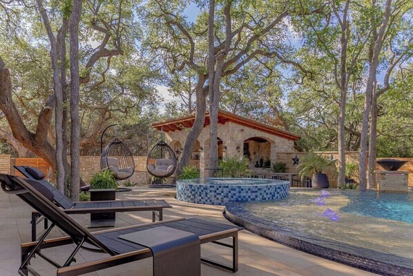 An outdoor pool area with lounge chairs, a hanging chair, and a tiled hot tub.