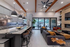 A modern kitchen with a central island, bar stools, and a dining area with a sofa and coffee table. - Luxury Retreat | Near Austin at Always on My Mind (Austin)