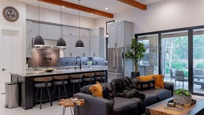 Una cocina moderna con una isla central, taburetes de bar y una zona de comedor con sofá y mesa de centro.