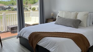 Quarto com cama grande, ventilador de teto e vista para uma varanda com corrimão.