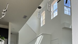 Ampla sala de estar com teto alto, escada e uma grande janela que permite entrada de luz natural.