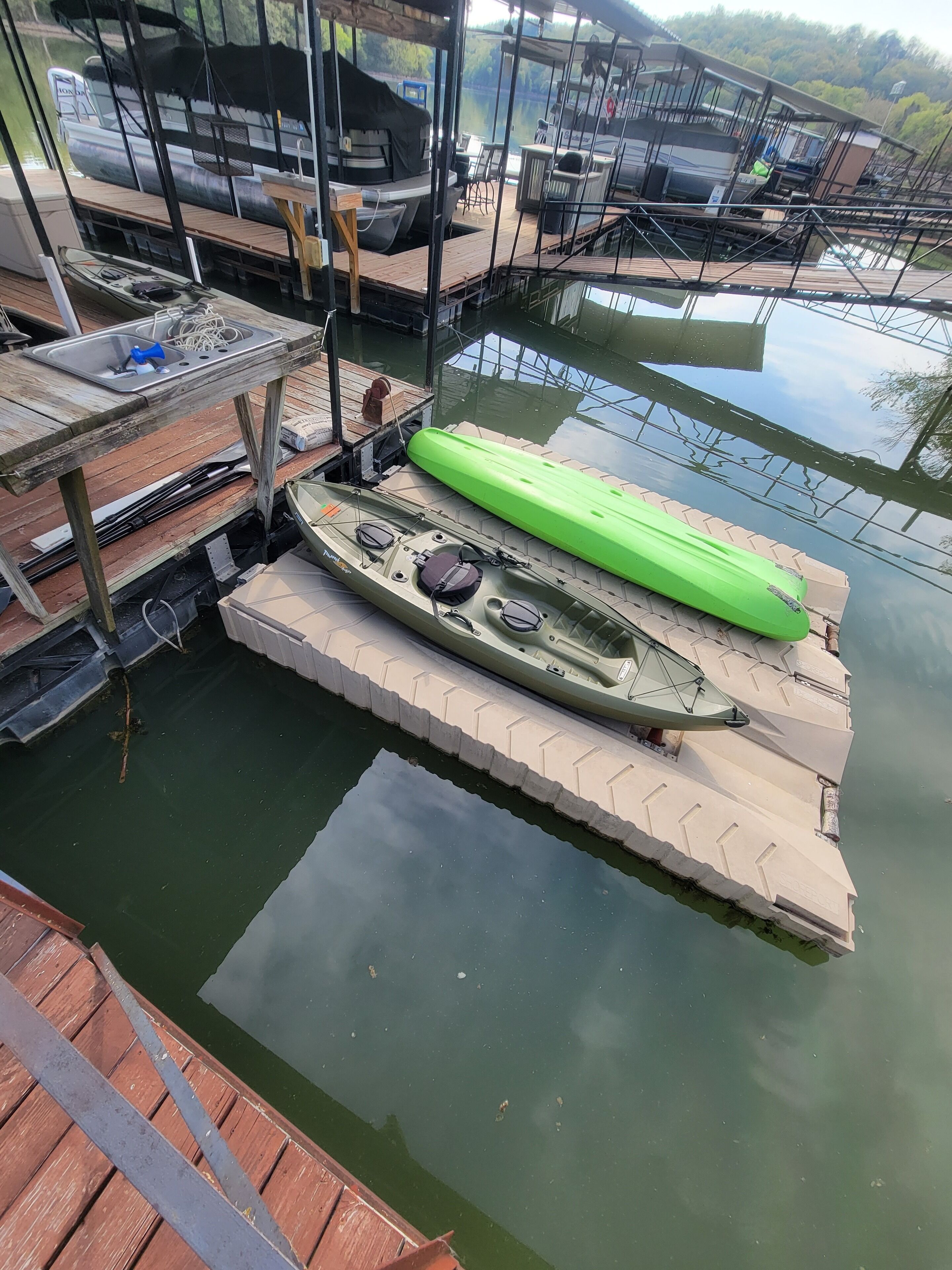 En dock med en kajak og et grønt paddleboard, træbænke og et metalgelænder.