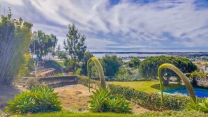 A landscaped garden with a swimming pool, a view of the sea, and a distant cityscape. - Ocean & Bay View Retreat | A/C & Private Yard (San Diego)