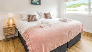 Un lit bien fait, recouvert d’une couverture rose, une lampe de chevet et un tableau accroché au mur.