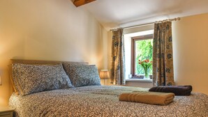 Un dormitorio con una cama grande, ropa de cama con estampado floral, una ventana con cortinas y un jarrón con flores.